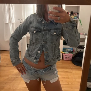 Ljusblå jeansjacka med knappar - Säljer en jättesnygg ljusblå jeansjacka med snygga sömmar och silverfärgade knappar. Jackan har två bröstfickor med lock och knappar, samt en figurnära passform. Perfekt att slänga över en t-shirt för en chill look. Den är helt ny utan prislapp!😍