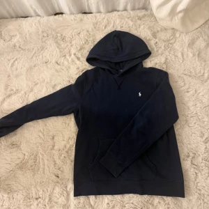 Mörkblå hoodie från Polo Ralph Lauren - Snygg mörkblå hoodie från Polo Ralph Lauren. Avänd fåtal gånger och i så bra skick. Säljer pga avänder nästan aldrig. Strl S/M