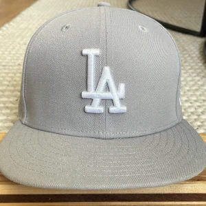 Grå LA keps  - Snygg grå 59FIFTY keps från New Era med LA Dodgers-logga broderad framtill i vitt. passar dig som vill ha en clean outfit med keps. Säljer för den är lite för liten för mitt huvud. Men är i väldigt bra skick. Storlek 6 7/8