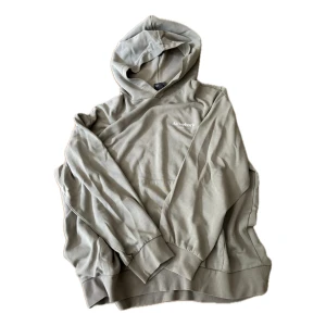 Beige hoodie från H&M XL - Snygg beige hoodie från H&M i relaxed fit. Tröjan har huva, långa ärmar och en liten vit logga på bröstet. Perfekt för en chill och avslappnad stil. Tillverkad i mjuk bomull som känns skön mot huden.