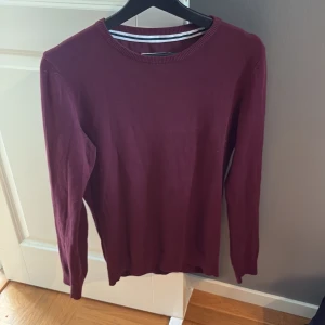 Vinröd tröja från Pier One - En stilren vinröd tröja från Pier One med rund halsringning och långa ärmar. Tröjan är i mjuk bomull och har en klassisk, enkel design som passar perfekt till jeans eller chinos. Snygg ribbad kant vid halsen för extra detalj.