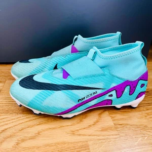 Nike Air Zoom fotbollsskor elite - Säljer ett par Nike Air Zoom fotbollsskor i en fräsch turkos färg och lila på sidan. Skorna har en strumpliknande passform, elastiskt band över vristen och är tillverkade i syntetmaterial för bästa grepp och känsla på planen.