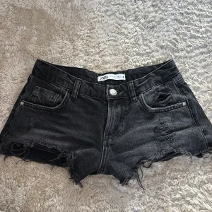 Svarta jeansshorts från Zara - Snygga svarta jeansshorts från Zara med råa, fransiga kanter och slitna detaljer framtill. Klassisk femficksmodell med låg midja och dragkedja.