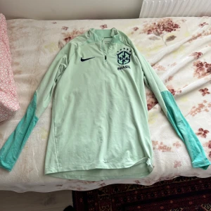 Nike Brasil långärmad träningströja - Kan mötas i malmö och frakta. Mintgrön långärmad träningströja från Nike med Brasil-logga och mörkare gröna detaljer på ärmarna. Tröjan har half zip, slim fit och är tillverkad i Dri-FIT-material. 