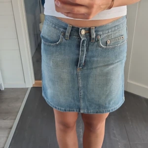 Jeanskjol från Kookai, storlek 36 - Snygg ljusblå jeanskjol från Kookai i klassisk femficksmodell. Kjolen är kort, har bälteshällor, knapp och dragkedja framtill samt coola bakfickor med dekorativa sömmar. Perfekt för dig som gillar en avslappnad och trendig stil.