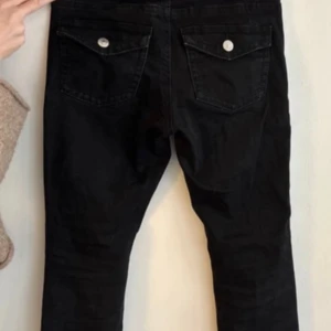 Svarta bootcut jeans med knapp där bak ifrån Gina Tricot  - Snygga svarta manchesterbyxor med raka ben och klassiska bakfickor med lock och silverfärgade knappar. Byxorna har en tidlös look och passar perfekt till en chill vardagsstil. Mjukt manchestertyg som ger en skön känsla och extra edge.