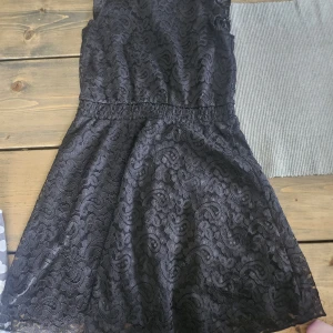 Svart spetsklänning med markerad midja - Supersnygg svart kortklänning i spets med markerad midja och lätt utställd kjol. Klänningen har ett vackert spetsmönster över hela plagget och är perfekt för dig som gillar en elegant och trendig look.