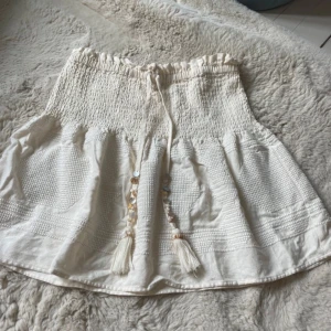 Vit bandeau tubtopp med knytband - Supersöt vit kjol som också kan användas som  topp med smock upptill och dekorativa knytband med pärlor och tofsar framtill.  I mycket bra skick