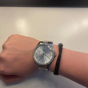 Silverfärgad klocka från Regal - Stilren klocka från Regal i silverfärg med metallarmband och glittrande stenar runt urtavlan. Den är i väldigt bra skick, använt 1-2 gånger och ser ut som ny! Perfekt accessoar för dig som gillar en clean och snygg look.