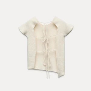 Vit stickad topp med snörning - Supermjuk och fluffig vit stickad topp med korta ärmar och snygg snörning i ryggen. Den har en clean, enkel look fram och coola knytband bak som ger en unik vibe. Perfekt för dig som gillar trendiga detaljer och vill ha något som sticker ut.