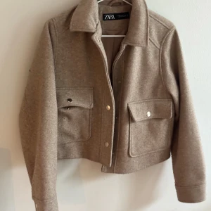 Beige jacka från Zara i ullmix - Snygg beige jacka från Zara med stora fickor framtill och coola metallknappar. Jackan har klassisk krage och är tillverkad i en mjuk ullmix som ger en lyxig känsla. Perfekt att slänga över en hoodie eller t-shirt för en chill look.