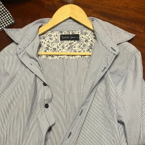 Randig skjorta från Solid Jeans - Snygg skjorta från Solid Jeans med tunna blå och vita ränder. Skjortan har klassisk krage, långa ärmar och knappar framtill. Insidan av kragen har ett blommigt tyg i blått och vitt som ger en unik touch. Perfekt för dig som gillar stilrena detaljer. Hör av vid frågor!🙌🏽 Alltid öppen till prisförslag!