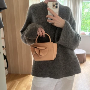 ATP Atelier Montalcino Rose Mini Handbag Magnolia - Superfin peach handväska från ATP Atelier i slätt skinn. Väskan har ett stilrent handtag och en stor dekorativ rosett framtill. Magnetlås och möjlighet att fästa axelrem. Perfekt storlek för det viktigaste och en snygg detalj till din outfit.
