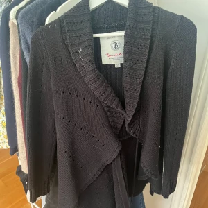 Svart stickad kofta från Bondelid XS - Mysig svart stickad kofta från Bondelid i storlek XS. Koftan har en bred krage, knytband i midjan och fina stickade detaljer. Den är begagnad men jag har själv aldrig använt den och den är i nyskick utan några defekter🩷