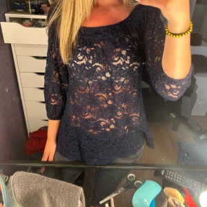 Mörkblå spetsblus med trekvartsärm - Säljer en mörkblå blus i spets med blommigt mönster och trekvartsärmar. Blusen har en lös passform och rundad halsringning. Perfekt för dig som gillar romantiska detaljer och vill ha en luftig topp med snygg struktur. Står stl 0, skulle säga att den skulle passa någon med xs-s