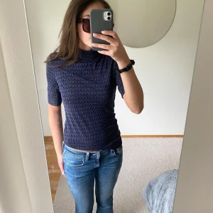 Mönstrad polotopp från Baum und Pferdgarten - Säljer en mörkblå polotopp från Baum und Pferdgarten med svart och vitt grafiskt mönster. Toppen har halvlång ärm, hög krage och är figurnära i modellen. Perfekt att styla med jeans eller kjol. Original pris 1100kr.