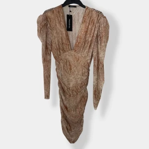 Beige mönstrad långklänning Trendyol - Supersnygg långklänning från Trendyol i beige och bruna toner med abstrakt mönster. Klänningen har v-ringning, långa ärmar med lätt puff och draperad effekt framtill. Tillverkad i ett lätt, flowy material som känns lyxigt och trendigt.