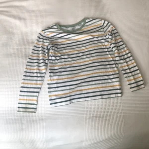 Randig långärmad tröja H&M barn - Superfin långärmad tröja från H&M i ekologisk bomull. Vit bas med gröna och gula ränder samt grön ribbad kant vid halsen. Perfekt för dig som gillar en chill och färgglad stil. Sitter skönt och passar till det mesta!