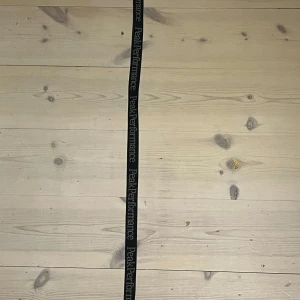 Svart Peak Performance bälte - Svart tygbälte från Peak Performance med vit logotyp längs hela bandet. Bältet har en stilren svart metallspänne och är justerbart för perfekt passform. Perfekt accessoar för en sportig och avslappnad look. Köpt ifrån PeakPerformance. Ny pris 550kr. Mitt pris 200kr 100cm