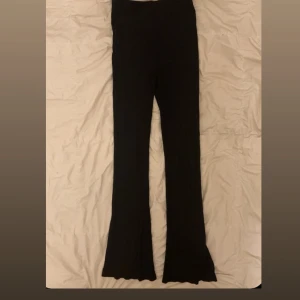 Svarta ribbade bootcut byxor - Svarta ribbade byxor med bootcut-modell och vågig kant längst ner. Byxorna har hög midja och är stretchiga, perfekta för en chill och trendig look.