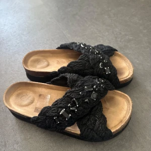 Svarta sandaler med flätad textil och pärlor - Snygga svarta sandaler med breda, flätade band i stickad textil och svarta pärlor som dekoration. Mjuk innersula i beige och platt sula för skön komfort. Perfekta för varma dagar när du vill ha något både coolt och bekvämt.