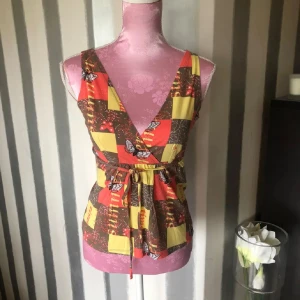 Färgglad omlottopp med fjärilar - Säljer en unik omlottopp i bomull med färgstarkt rutmönster i rött, gult och brunt. Toppen har v-ringning både fram och bak, knyt i midjan och är ärmlös. Dekorerad med fjärilar och små detaljer som gör den extra speciell. Perfekt för dig som gillar statement-plagg!