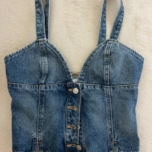 Jeans korsettopp från Zara - Säljer en snygg jeans korsettopp från Zara med breda axelband och knappar framtill. 