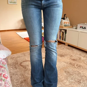 Blå bootcut jeans med slitningar - Snygga blå jeans med bootcut-modell och slitna detaljer vid knäna. Jeansen har klassisk femficksdesign och är tillverkade i denim med en lätt tvättad look. Perfekta för en avslappnad och trendig stil.