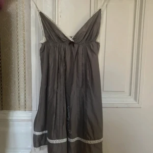 Grå Odd Molly klänning med spets - Säljer denna supersöta grå kortklänningen från Odd Molly med tunna axelband, vit spetskant och broderade detaljer både fram och bak. Klänningen har v-ringning och fina broderier nertill samt en broderad ros på ryggen. Perfekt för dig som gillar unika detaljer och romantisk stil.