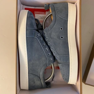  Feta Christian Louboutin skor - Snygga blå sneakers i mocka från Christian Louboutin med klassisk röd sula och vita kanter. Skorna har rund tå, snörning och en stilren design som sticker ut med den ikoniska röda undersidan. Perfekta för dig som vill ha något exklusivt och trendigt. Hör av dig vid funderingar// MVH Jack