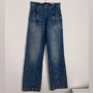 Högmidjade jeans från Scotch & Soda - Super snygga jeans från Scotch & Soda med hög midja och raka, lite vidare ben. Snygga guldknappar framtill i dubbla rader och coola sömdetaljer längs benen. 