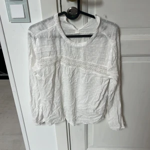 Vit blus med spets från ONLY - Säljer en söt vit blus från ONLY med diskret prickigt mönster och fina spetsdetaljer över bröstet. Blusen har lång ärm och är tillverkad i ett lätt och luftigt bomullstyg. Perfekt för dig som gillar romantisk och stilren look.