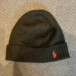 Svart stickad mössa Polo Ralph Lauren - Svart ribbstickad mössa från Polo Ralph Lauren. 