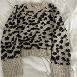 Beige leopardmönstrad stickad tröja - Supermjuk stickad tröja i beige med svart leopardmönster. Tröjan har breda ribbade muddar och rund halsringning. 