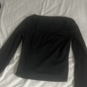 Svart långärmad topp med vid ringning - En stilren svart långärmad topp med bred, rundad ringning. Snygg och enkel att matcha till olika outfits. Passformen är normal och materialet känns mjukt mot huden.
