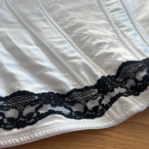 Vit korsettopp  - Säljer en vit korsettopp från H&M med svarta spetsdetaljer och rosett framtill🖤storlek 40 på bysten men passar S!
