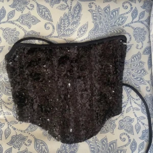 Svart paljettkorsett med snörning - Supersnygg svart korsett topp täckt av glittriga paljetter. Toppen är axelbandslös och har snörning i ryggen för perfekt passform. Perfekt för att sticka ut och ge extra edge till din outfit.