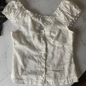 Vit topp med broderade blommor - Supersöt vit topp med broderade blommor och volangdetaljer vid ärmar och nederkant. Perfekt för sommaren ☀️🩷