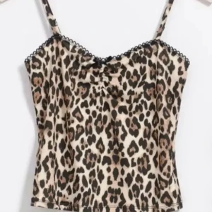 Leopardmönstrad linnetopp med spets - Säljer en leopardmönstrad linnetopp med tunna axelband och söt svart spetskant upptill. Toppen har en liten rosett framtill och rynkdetalj vid bysten. Materialet är mjukt och stretchigt, perfekt för en trendig look. Bara använd 2 ggr