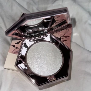 Fenty Beauty Diamond Bomb Highlighter - How Many Carats? från Fenty Beauty. En superglittrig highlighter med silvrig, diamantliknande finish. Kommer i en lyxig, sexkantig spegelkompakt med roséguldsdetaljer. Perfekt för att ge ansiktet en intensiv glow. OANVÄND!! Säljer för fick som ptesent och  aldrig snvänding av den då jag inte gillar glitter!