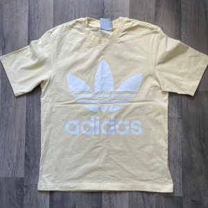 Adidas gul t-shirt med stor logga - Fräsch ljusgul t-shirt från Adidas i storlek M. Den är i oversized passform. Har bara haft på mig en till två gånger. Modellen är 167 cm lång, väger 63 kg. Längden 73 cm, axeln 48 cm