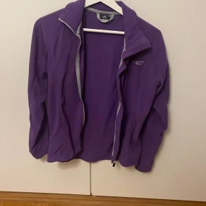 Lila fleecejacka från North Bend - Säljer en lila fleecejacka från North Bend i storlek 38. Jackan har hel dragkedja framtill, en bröstficka med dragkedja och hög krage. Perfekt för lager-på-lager och chill utomhus. Snygg och enkel design med grå detaljer vid dragkedjorna.
