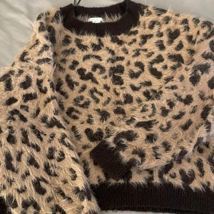 Beige fluffig leopardmönstrad tröja - Supermjuk och fluffig stickad tröja i beige med svart leopardmönster. Perfekt för dig som vill sticka ut med en trendig och cozy look.
