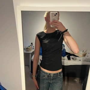 Svart ärmlös topp i bomull - Säljer en svart, tight och croppad ärmlös topp med rund halsringning. Draperad på sidan och går att ha vid festliga tillfällen lika väl som till vardags🩷.