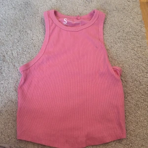 Rosa ribbad tanktopp - Säljer en rosa ribbad linnetopp i ärmlös modell. Toppen har en rund halsringning och croppad passform, perfekt till jeans eller kjol. Enkel och stilren design som är lätt att matcha med andra plagg.