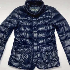 Mörkblå dunjacka från Herno - Snygg mörkblå dunjacka från Herno med quiltad design och två stora fickor framtill. Jackan har hög krage och stängs med knappar. Lätt och smidig, perfekt för kyliga dagar. Fylld med ultralätt gåsdun för extra värme utan att kännas tung.