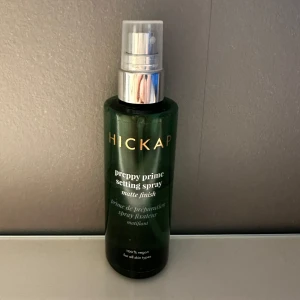 Hickap Preppy Prime Setting Spray - Preppy Prime Setting Spray från Hickap med matt finish. Kommer i en mörkgrön plastflaska med spraymunstycke i silver. 100% vegansk och passar alla hudtyper. Perfekt för att fixera sminket och ge en fräsch look. Flaskan är halvfull
