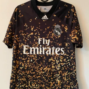 limited edition t shirt real madrid konfetti 19/20 - Snygg Real Madrid fotbollströja från Adidas i svart med guldigt konfettimönster. Tröjan har korta ärmar, rund hals och är tillverkad i lätt och ventilerande Climalite-material. Perfekt för dig som vill sticka ut på planen eller på läktaren. 