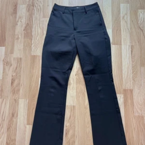 Svarta kostymbyxor BikBok - Svarta kostymbyxor från BikBok i klassisk rak/bootcut modell. Byxorna har hällor för bälte, dold dragkedja och knapp framtill. Snygg passform med raka ben som får en lätt utsvängd siluett. Perfekta för en clean och stilren look.