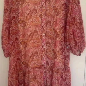 Paisleymönstrad klänning Gina Tricot - Paisleymönstrad klänning från Gina Tricot i rosa, orange och bruna toner. Modellen har knappar framtill, trekvartsärmar med resår och en luftig passform. Perfekt för dig som gillar boho-vibbar och färg. Superfin till sneakers eller boots!